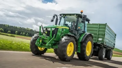 Zelený traktor John Deere táhne zemědělský přívěs po silnici
