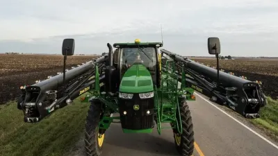 Zelený samojízdný postřikovač John Deere se složenými rameny na cestě.