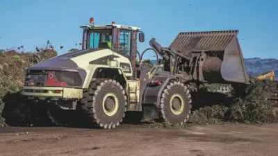 Světle zelený hybridní kolový nakladač Volvo LX1 s naloženou lžící na skládce.