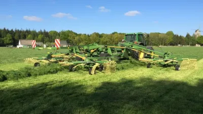 Traktor se širokým shrnovačem Krone na louce