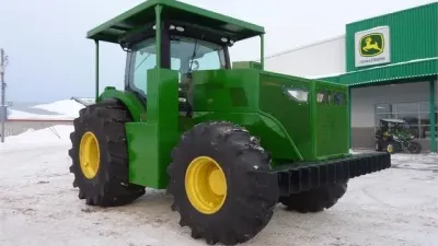 Zelený zakrytovaný lesní traktor John Deere s velkými pneumatikami na sněhu.