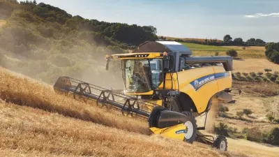 Žlutá sklízecí mlátička New Holland sklízí obilí ve svahu