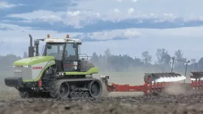 Zelenobílý pásový traktor Claas Challenger táhne pluh na poli.