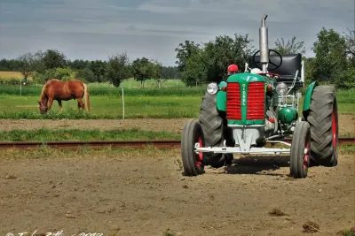 Historický zelený traktor Zetor na poli, v pozadí kůň