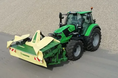 Zelený traktor s čelním žacím strojem Krone EasyCut F 400 CV Fold na silnici