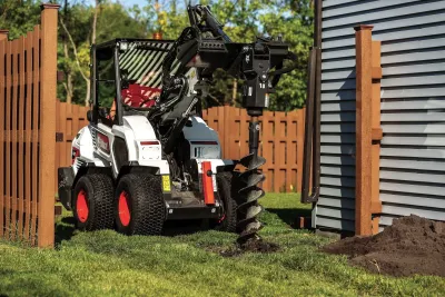 Bílý kloubový nakladač Bobcat L28 s vrtacím nástavcem na zahradě