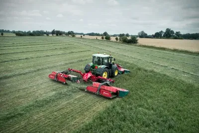 Traktor s červenou žací trojkombinací Kverneland na louce