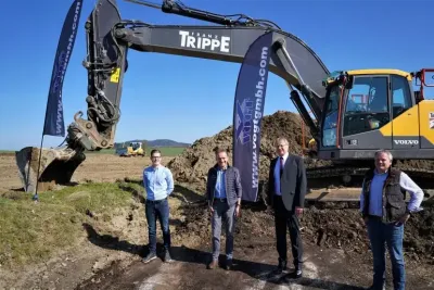 Čtyři muži stojí před pásovým rypadlem na staveništi