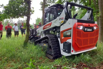Pásový nakladač Bobcat při předvádění mezi stromy.
