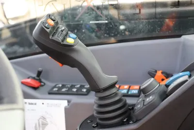 Nový joystick je opatřen tlačítky pro ovládání funkcí výložníku, přídavné hydrauliky a nových chytrých funkcí, jako jsou Auto Grab, funkce vyklepání lopaty, plovoucí poloha výložníku, systém řazení rychlostí a volba směru jízdy.