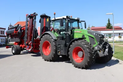 Zelený traktor s červenou žací kombinací SIP stojí před výrobním závodem.