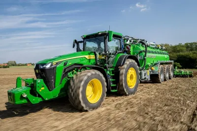 Zelený traktor John Deere s velkými pneumatikami Continental táhne cisternu na poli.