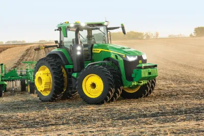 Zelený traktor John Deere s kultivátorem na poli