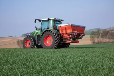 Zelený traktor s červeným rozmetadlem hnojiv Rauch Axis na poli