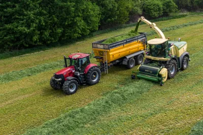 Sklízecí řezačka Krone vedle traktoru s návěsem na louce
