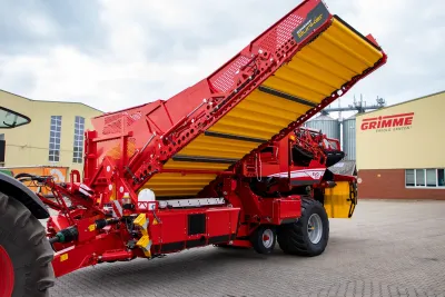 Červený vyorávač Grimme EVO 280 se zvednutým zásobníkem před závodem Grimme.