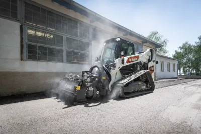 Pásový kompaktní nakladač Bobcat pracuje u budovy.