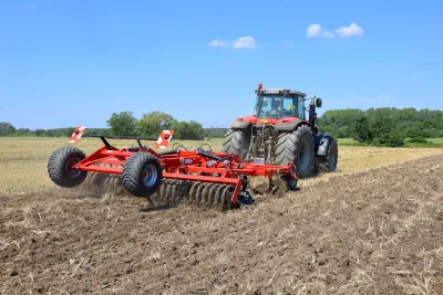 Traktor s červeným diskovým podmítačem SMS CZ ATOS na poli.