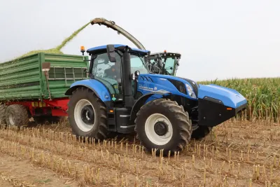 Modrý traktor New Holland při odvozu zelené hmoty od řezačky.