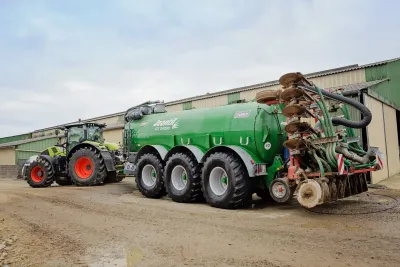 Traktor s velkou zelenou cisternou na dvoře.