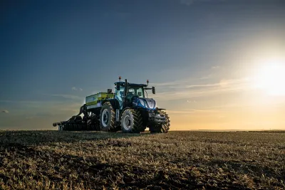 Modrý traktor New Holland T7.300 na poli za západu slunce.