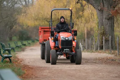 Řidič na oranžovém malotraktoru Kubota s přívěsem.