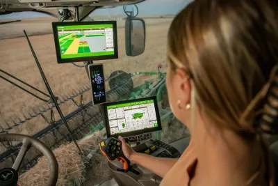 Řidička sleduje monitory John Deere v kabině stroje.