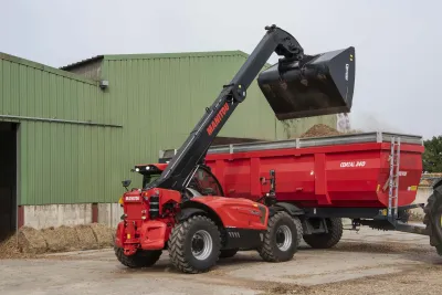 Manipulátor Manitou nakládá materiál do červeného vozu.