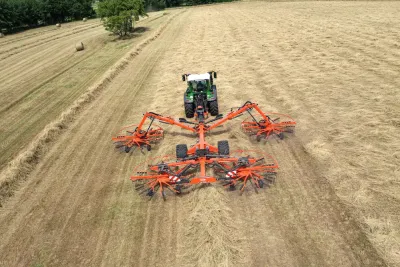 Traktor se čtyřrotorovým shrnovačem Kuhn při práci na louce