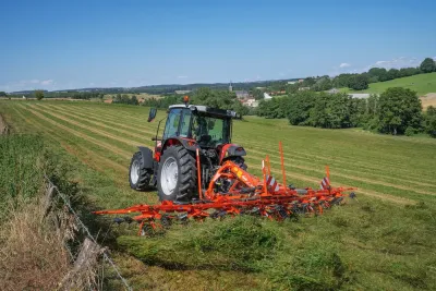 Traktor s oranžovým obracečem Kuhn na louce