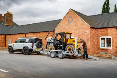 Malý žlutý manipulátor JCB na přívěsu za bílým automobilem