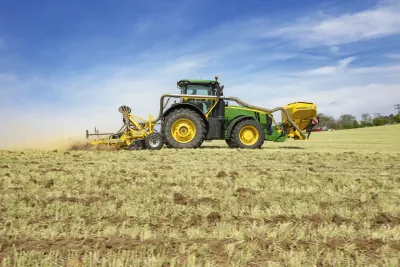 Zelený traktor s kypřičem BEDNAR při práci na poli