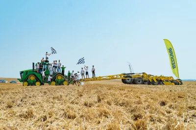 Pásový traktor táhne žlutý podmítač BEDNAR, lidé oslavují rekord na poli
