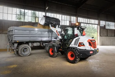 Kolový nakladač Bobcat L95 nakládá obilí na přívěs v hale