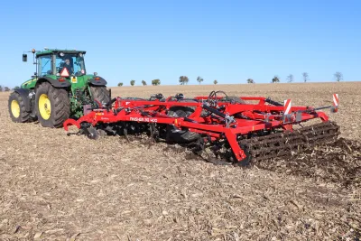 Zelený traktor John Deere s červeným kypřičem SMS CZ Finisher na poli