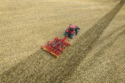 Traktor táhne červený stroj Väderstad na poli