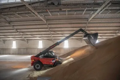 Červený teleskopický manipulátor Manitou nakládá obilí ve skladovací hale