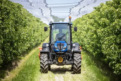 Modrý nízkoprofilový traktor New Holland projíždí ovocným sadem