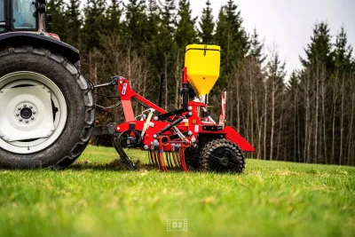 Traktor s výsevním strojem a žlutým zásobníkem na osivo provádí regeneraci travního porostu.
