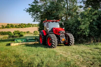 Červený traktor Zetor Řady 6 se žacím strojem na louce