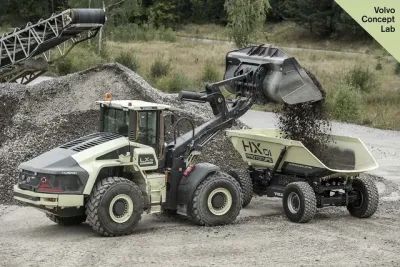 Hybridní nakladač Volvo LX1 vysypává materiál do autonomního vozíku.
