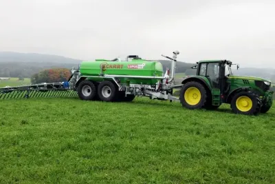 Zelená cisterna Eckart tažená traktorem John Deere na louce.