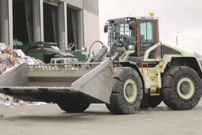 Nakladač Volvo LX1 s lžící u hromady odpadu.