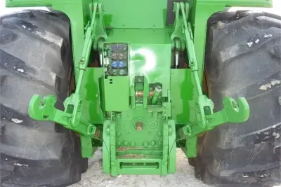 Zadní tříbodový závěs traktoru John Deere mezi lesními pneumatikami.