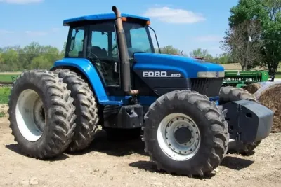 Modrý traktor Ford 8970 s dvojmontáží kol před budovou farmy.